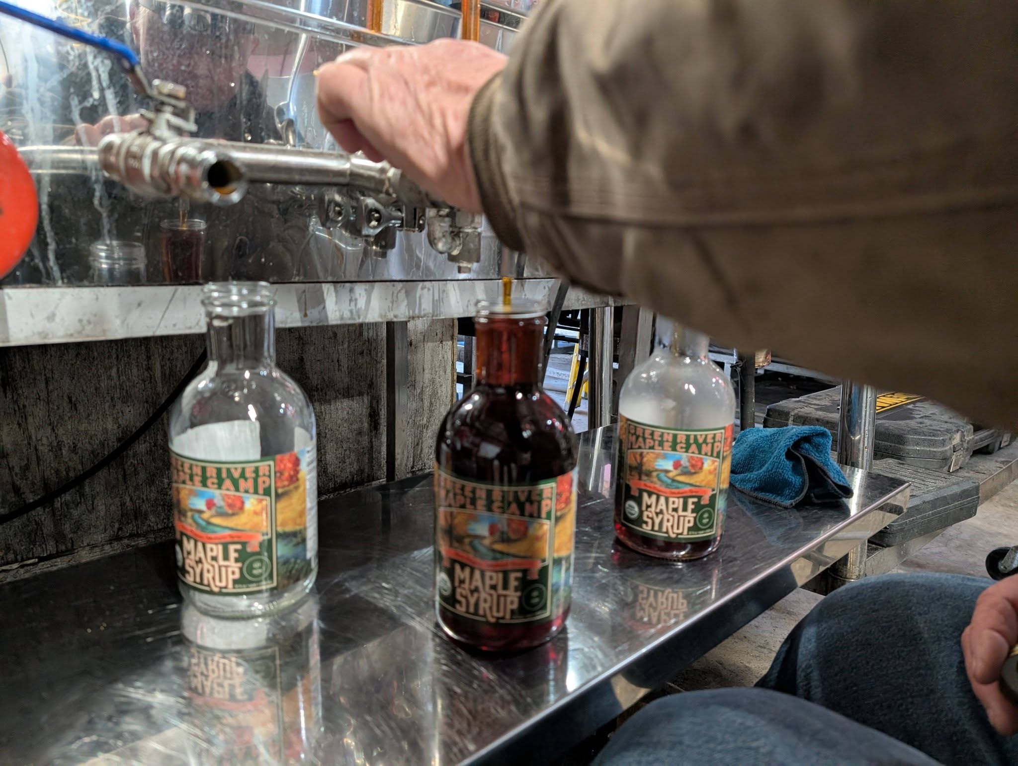 Filling labeled glass bottles of Green River maple syrup at the bottling tank